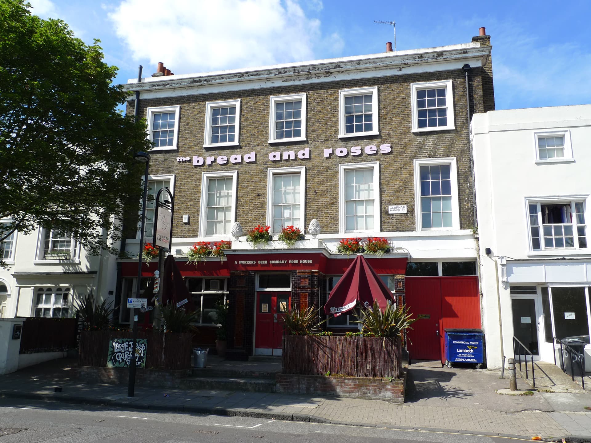 Brick Georgian pub frontage with red ground floor, flower boxes, umbrellas and the Bread and Roses name across the upper storey