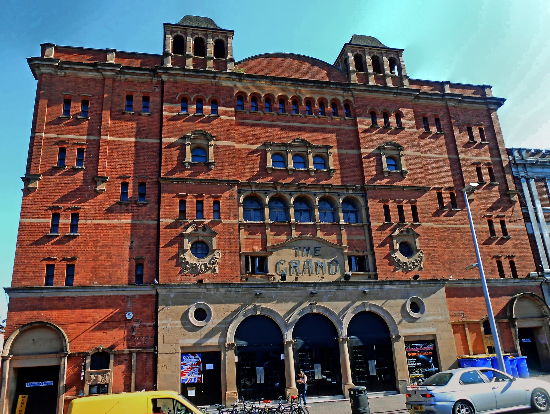 Red-brick Victorian theatre facade with towers and arched windows, The Grand lettering above a street entrance