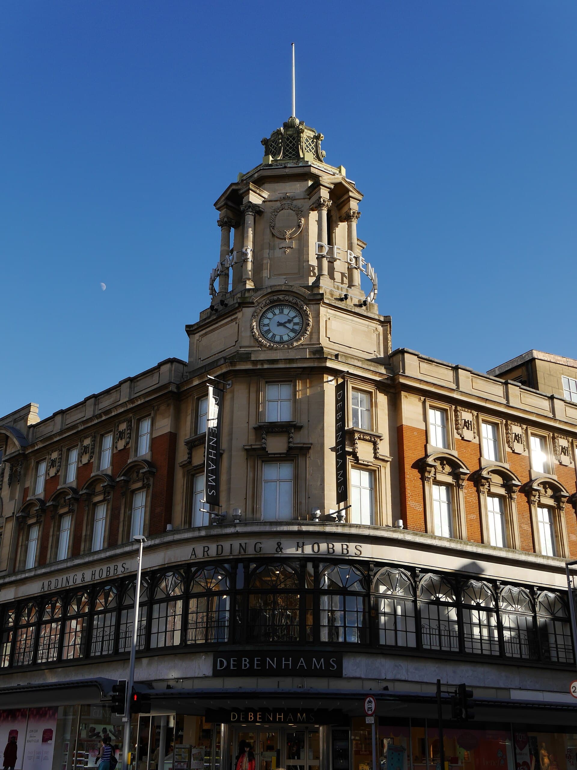 Corner of the Arding & Hobbs building with its clock tower, signed Debenhams, against a clear blue sky