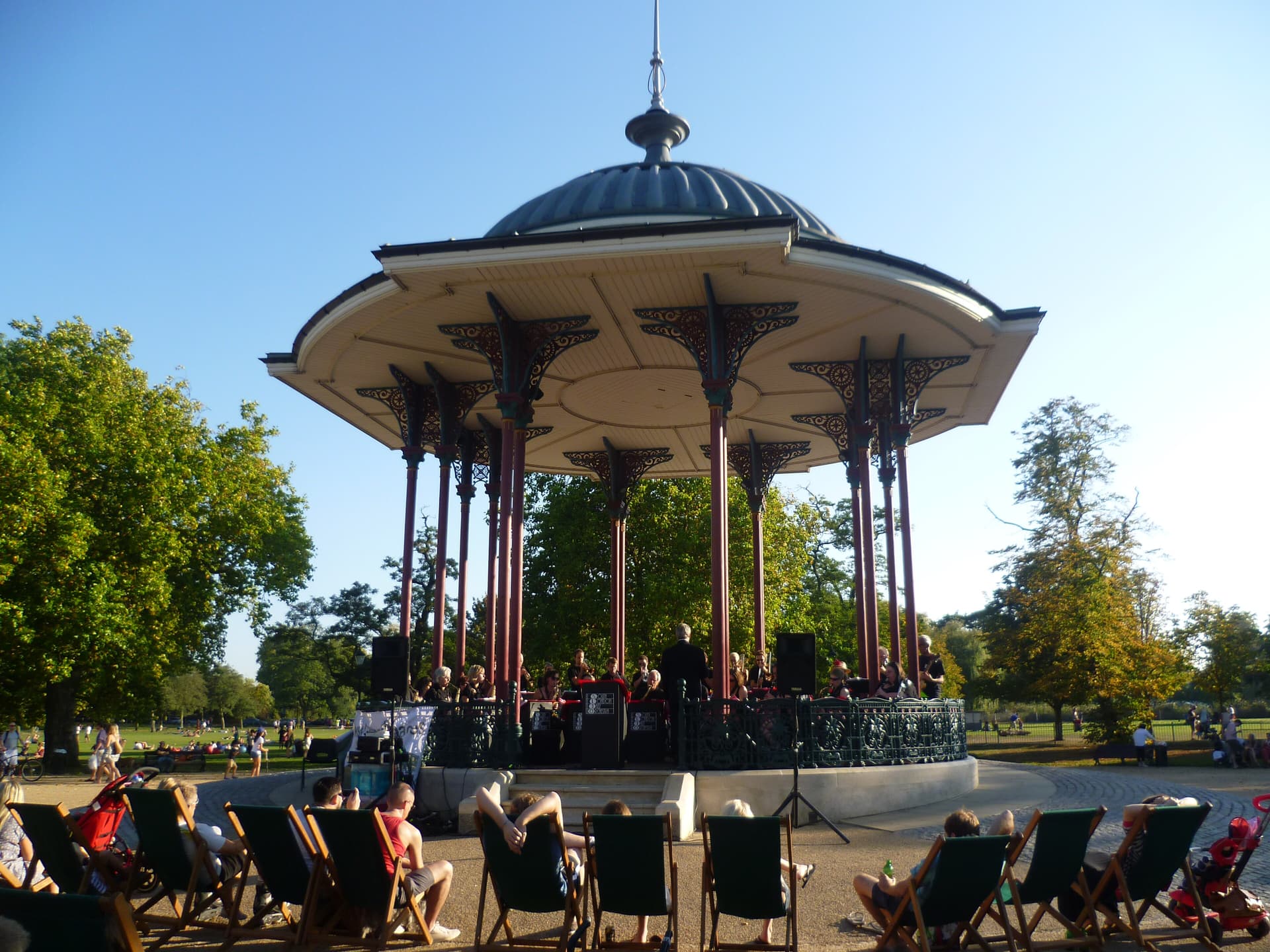 Band playing in the ornate Victorian bandstand on Clapham Common, with deckchairs in the foreground and sunbathers on the grass