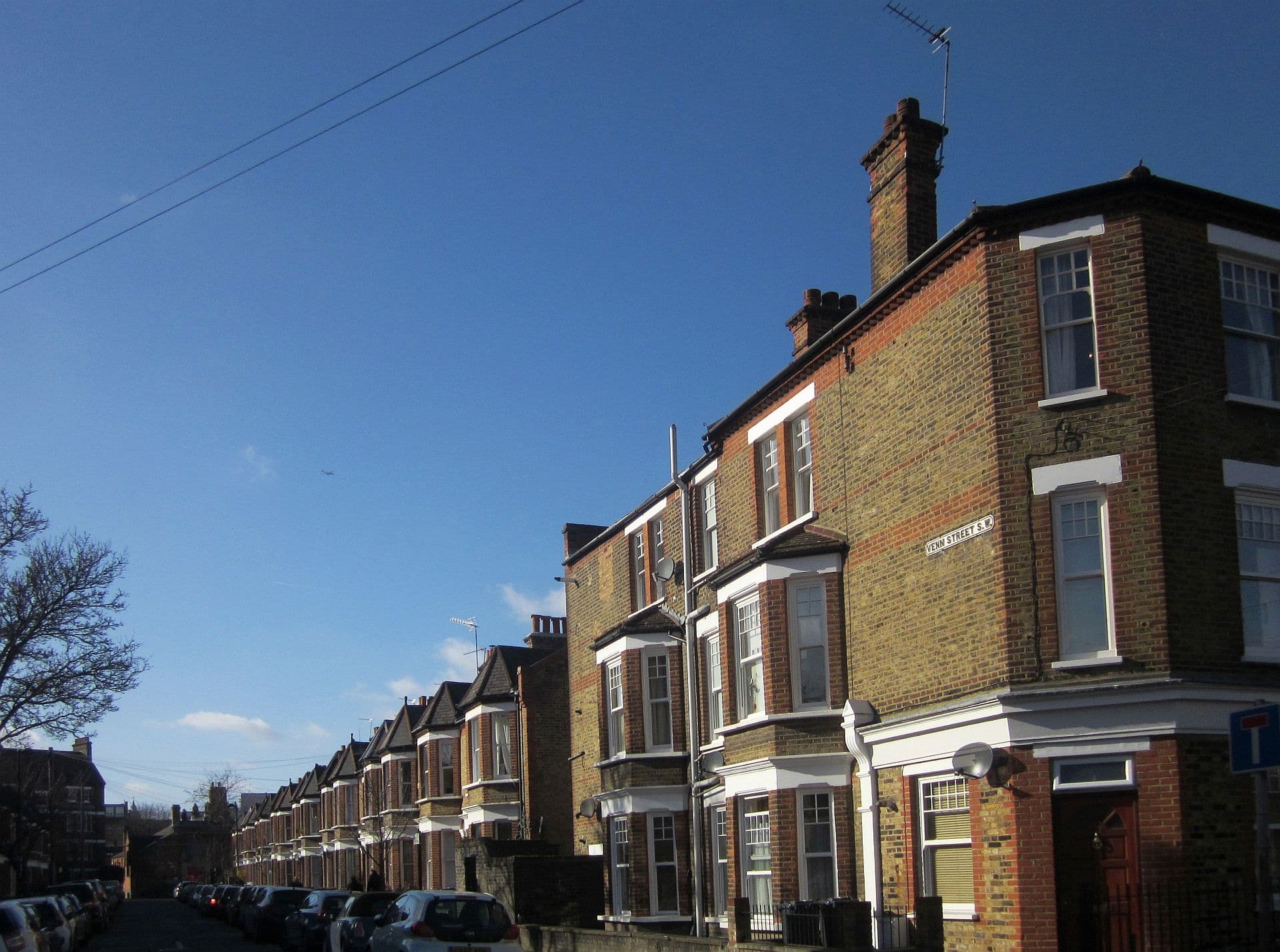 Sunlit Victorian brick terraced houses on Venn Street, Clapham, with parked cars and a deep blue sky