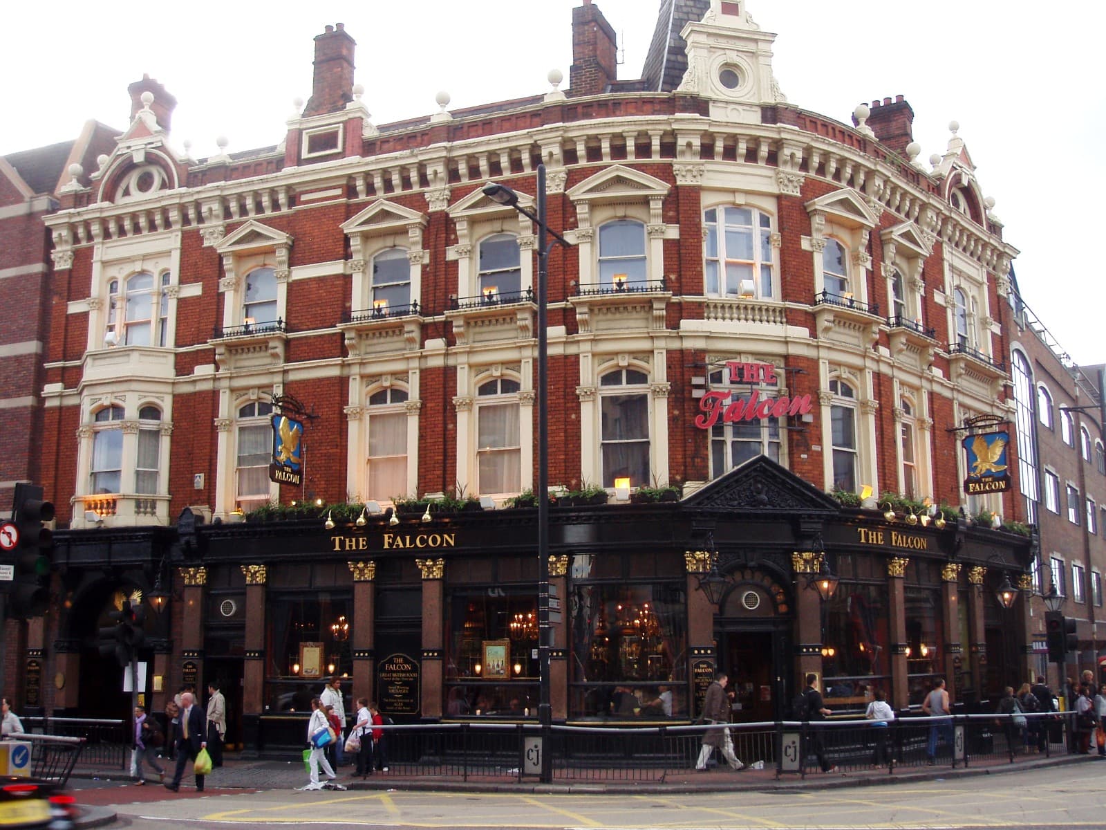 Ornate red-brick Victorian corner pub with The Falcon signage, black ground floor and pedestrians passing on the pavement