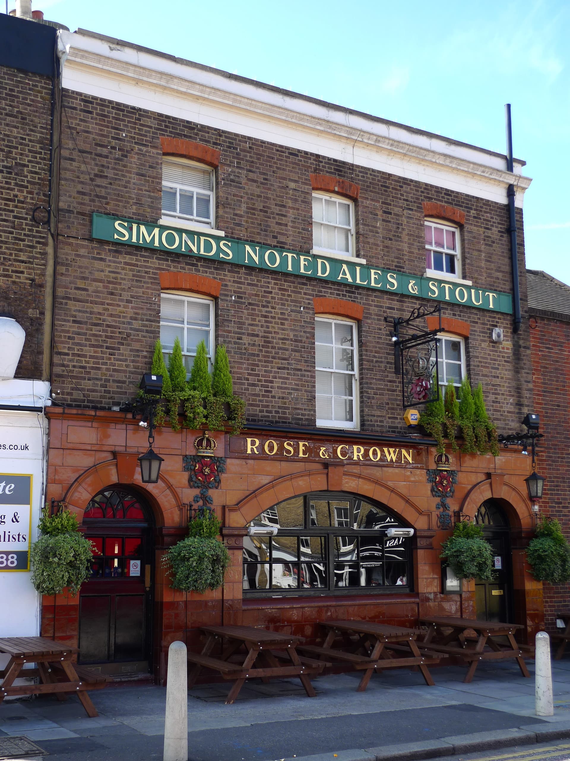 Terracotta-tiled front of the Rose & Crown pub with brick upper floors, hanging baskets and picnic benches outside