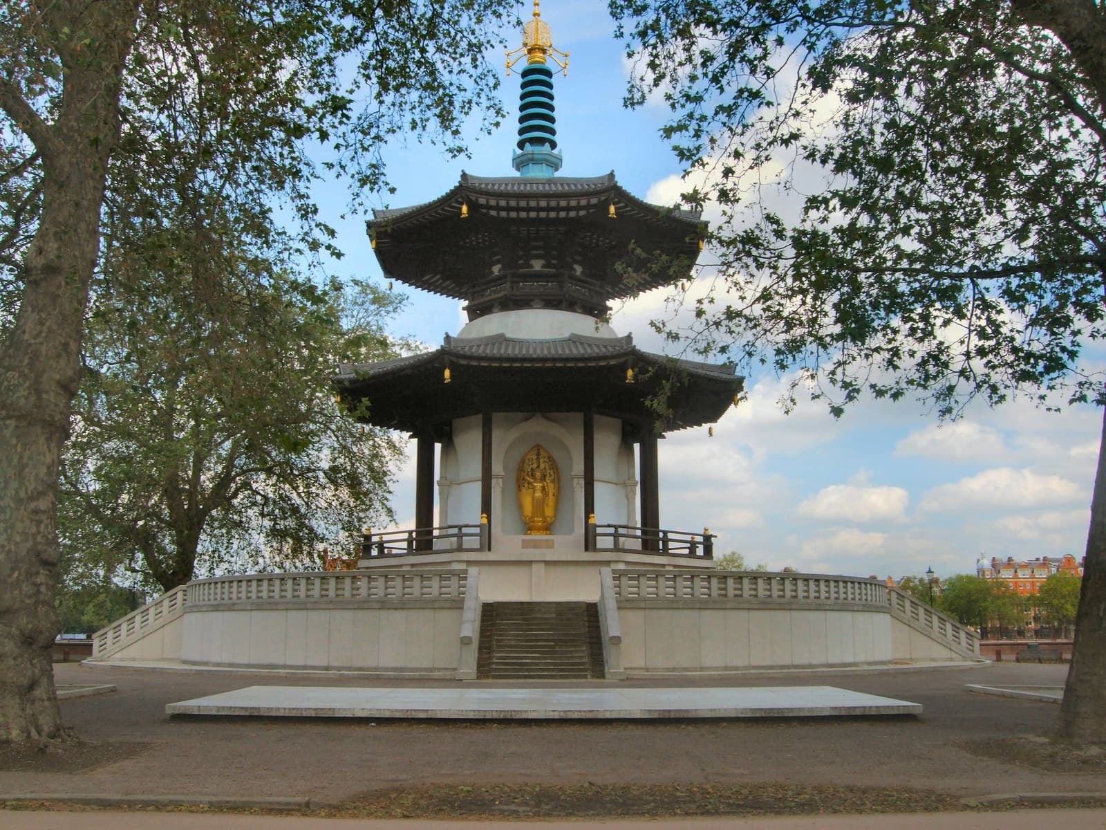 Battersea Park's Peace Pagoda with gilded Buddha figure, framed by plane trees under a blue sky