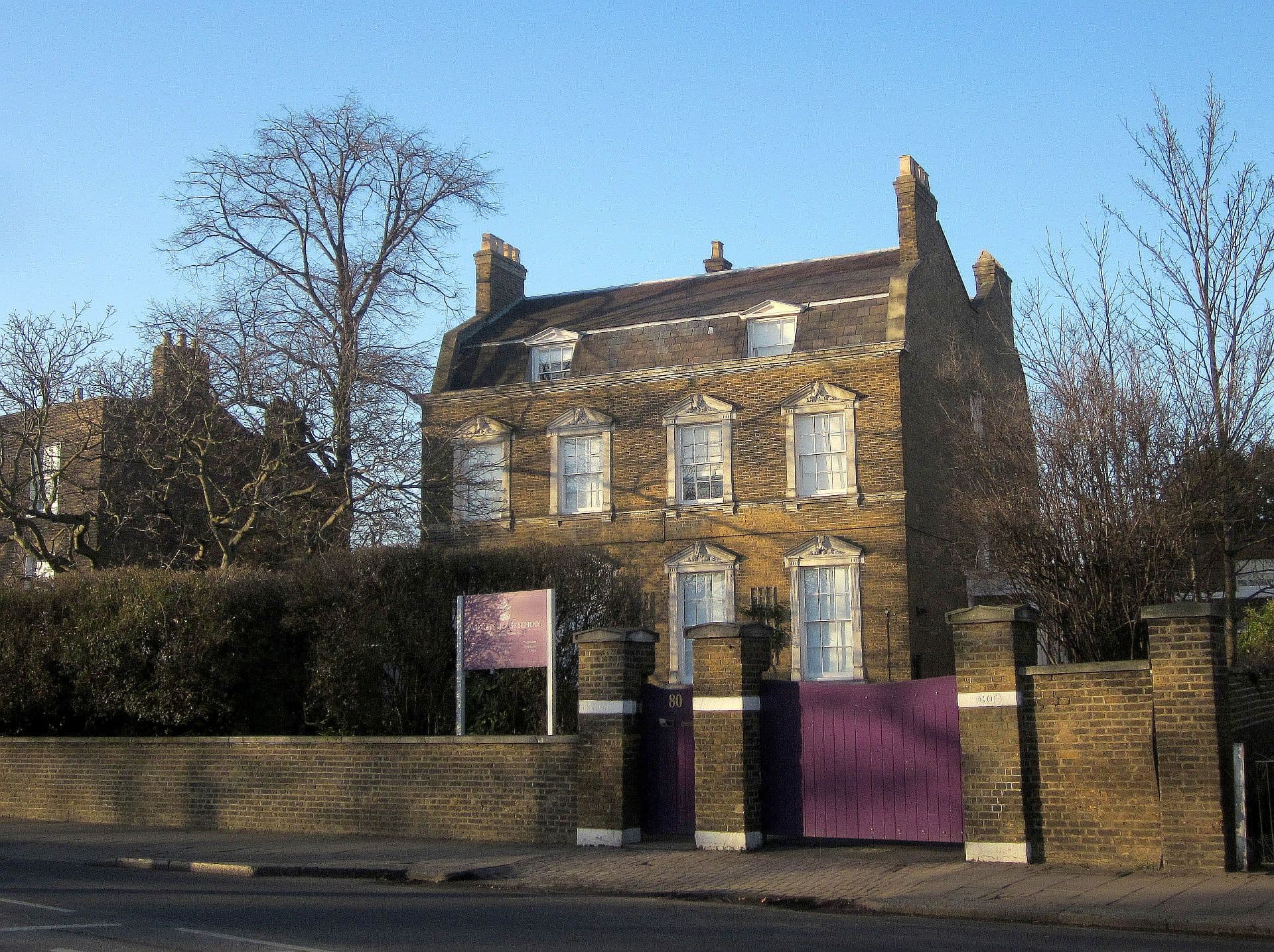 Georgian yellow-brick house with pedimented sash windows behind a brick wall and purple gates on a London street