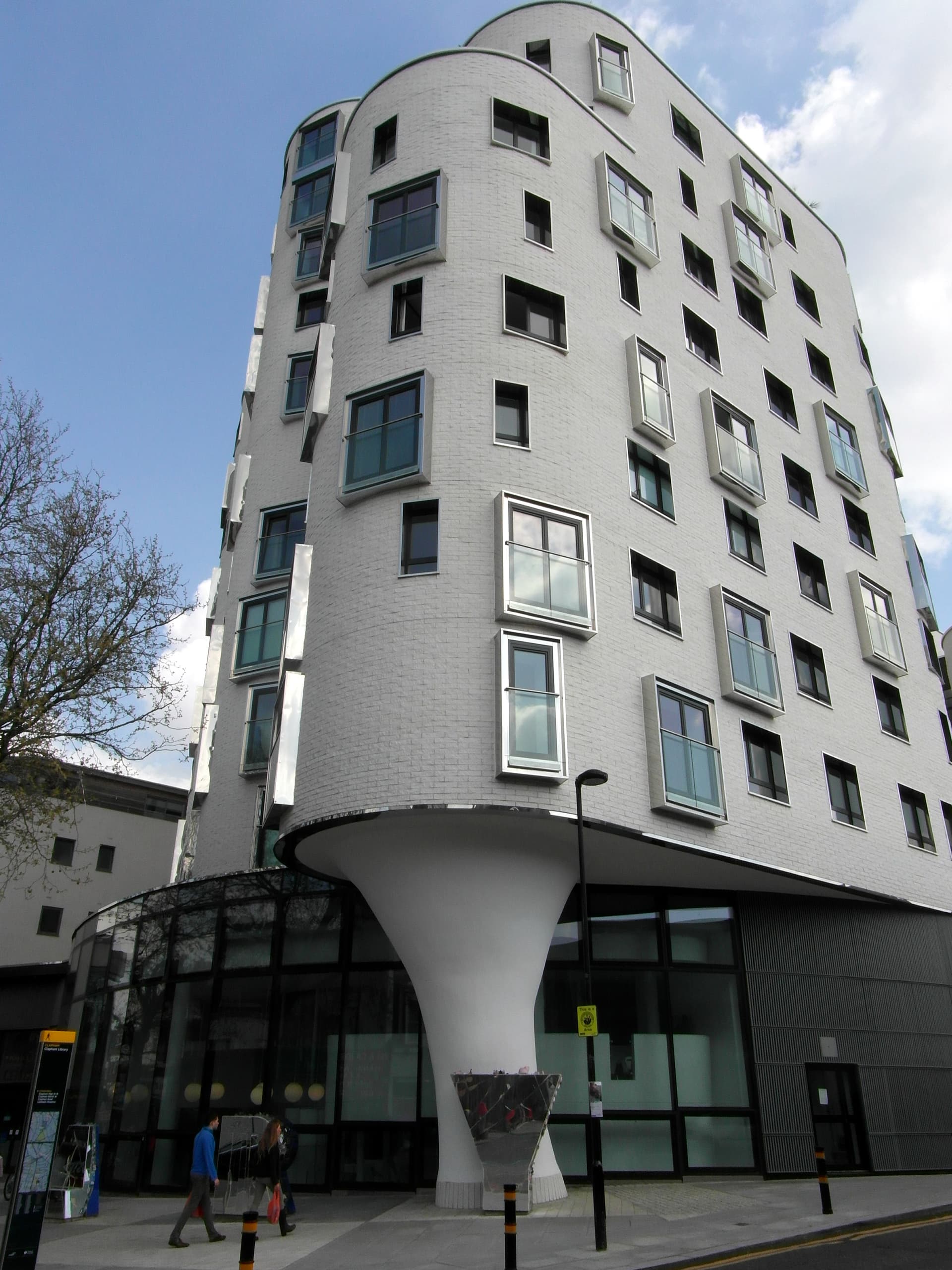 White curved brick apartment block on a funnel-shaped column above a glazed ground floor, Clapham High Street